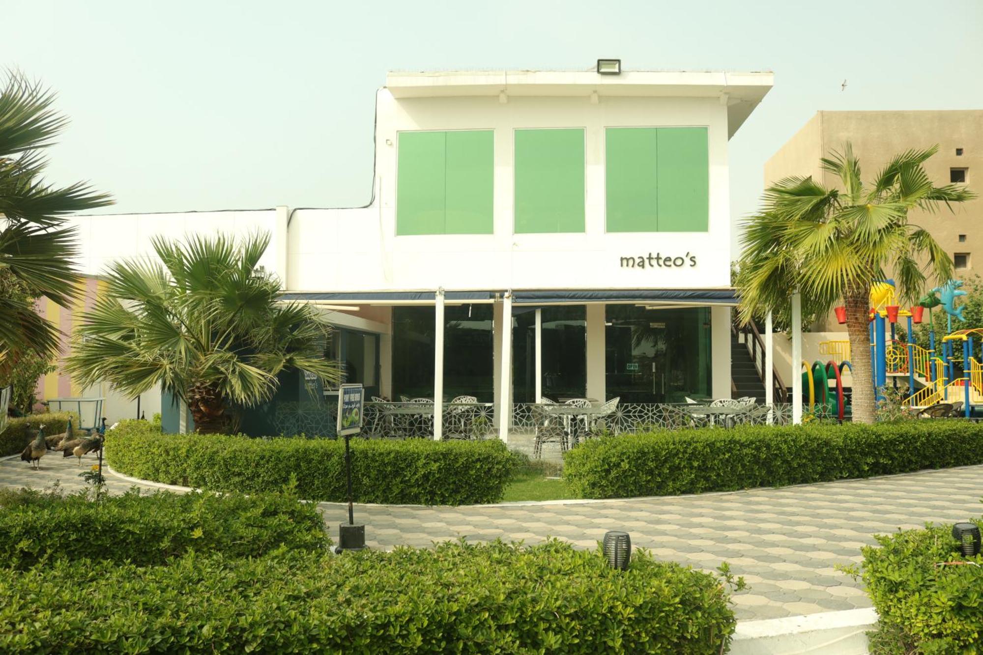 Lagoona Beach Luxury Resort And Spa Манама Екстериор снимка The photo shows a building with the name "matteo's" displayed prominently on the front. The structure features large windows and green shutters. There is a landscaped area in front with bushes and palm trees, along with a paved pathway leading up to 