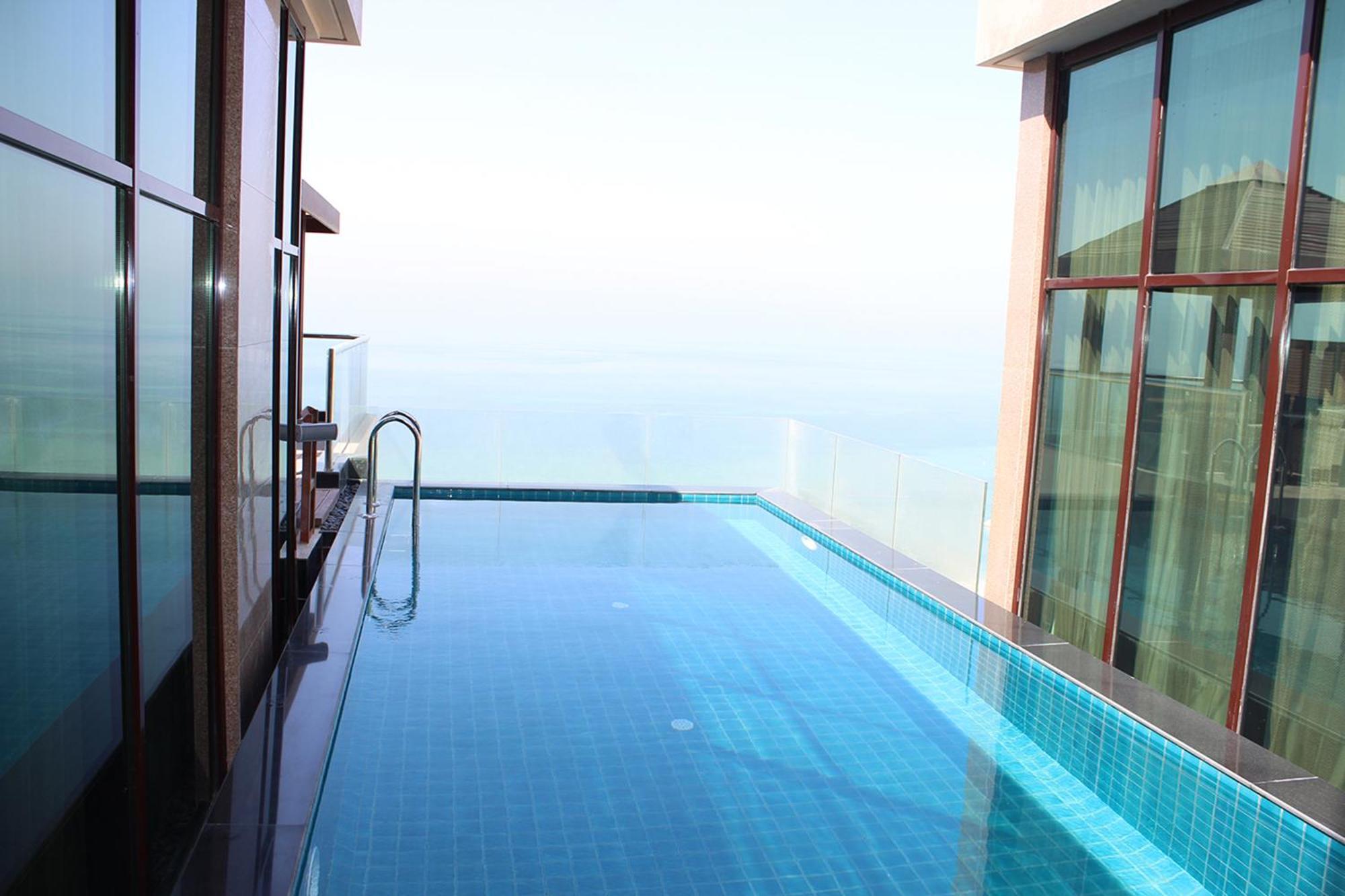 Lagoona Beach Luxury Resort And Spa Манама Екстериор снимка The photo shows an infinity pool situated on a balcony or rooftop, with a clear view extending to the horizon. The pool has a sleek design with blue tiles, and it appears to be reflecting the sky. There is a ladder on one side for access into the poo