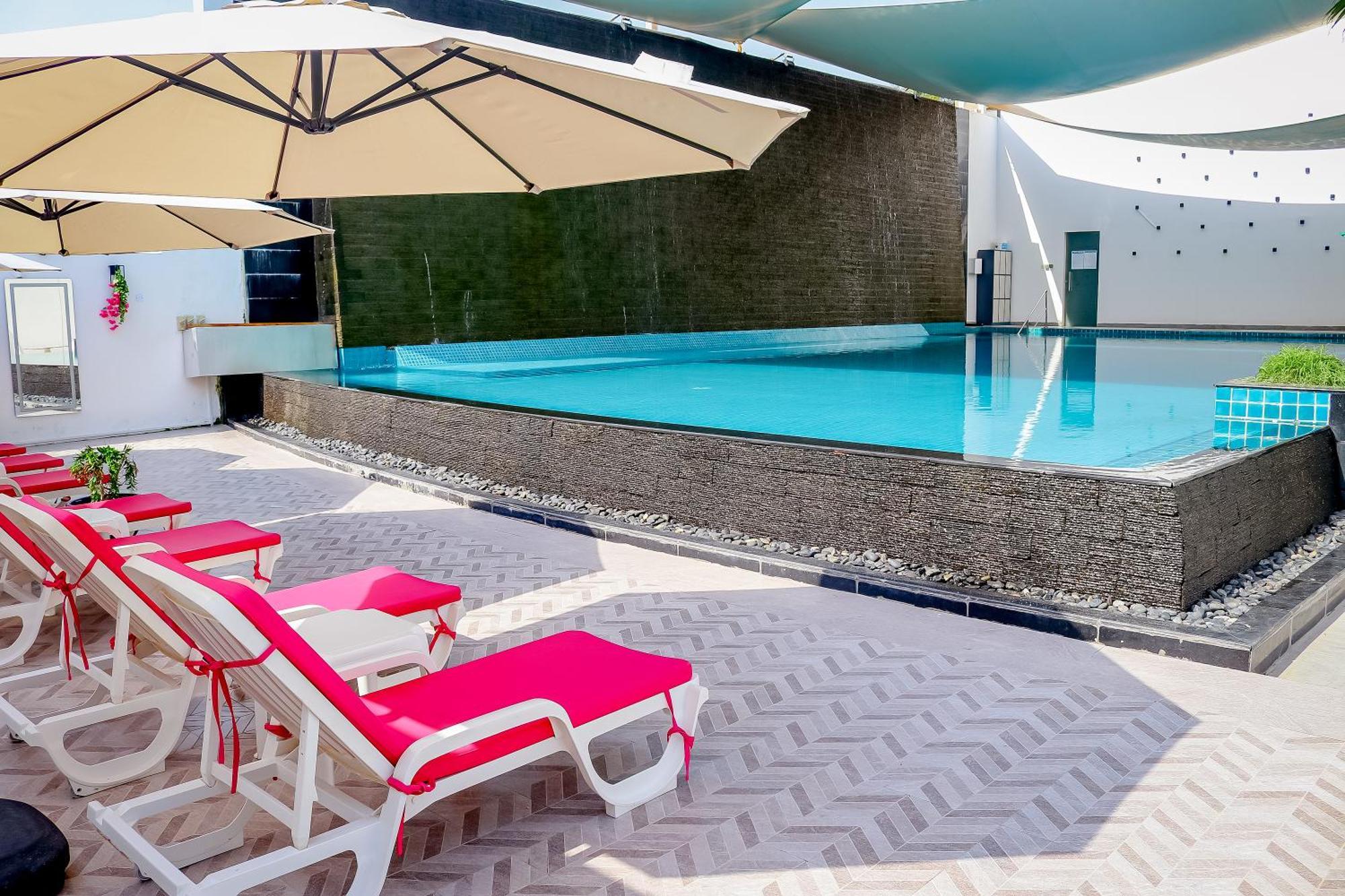 Lagoona Beach Luxury Resort And Spa Манама Екстериор снимка The photo shows a pool area featuring a rectangular swimming pool with clear blue water. Surrounding the pool are light-colored lounge chairs with pink cushions, positioned under large umbrellas for shade. The pool is bordered by a textured wall, and