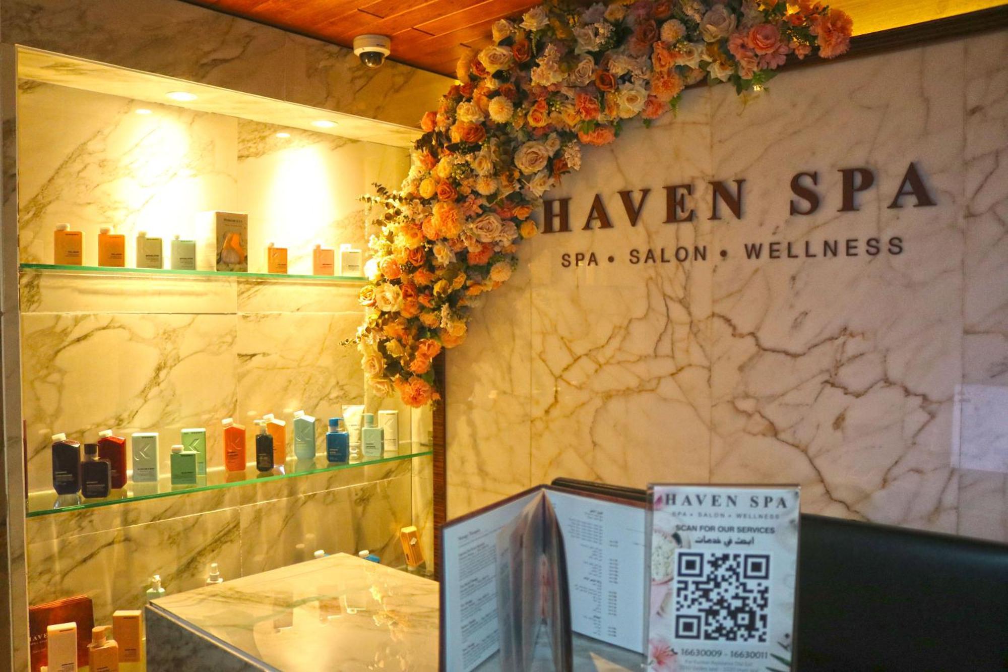 Lagoona Beach Luxury Resort And Spa Манама Екстериор снимка The photo shows the interior of a spa called "Haven Spa." The wall is decorated with beautiful artificial flowers, creating an inviting atmosphere. There are several shelves displaying various colorful bottles and products, likely for skincare or wel