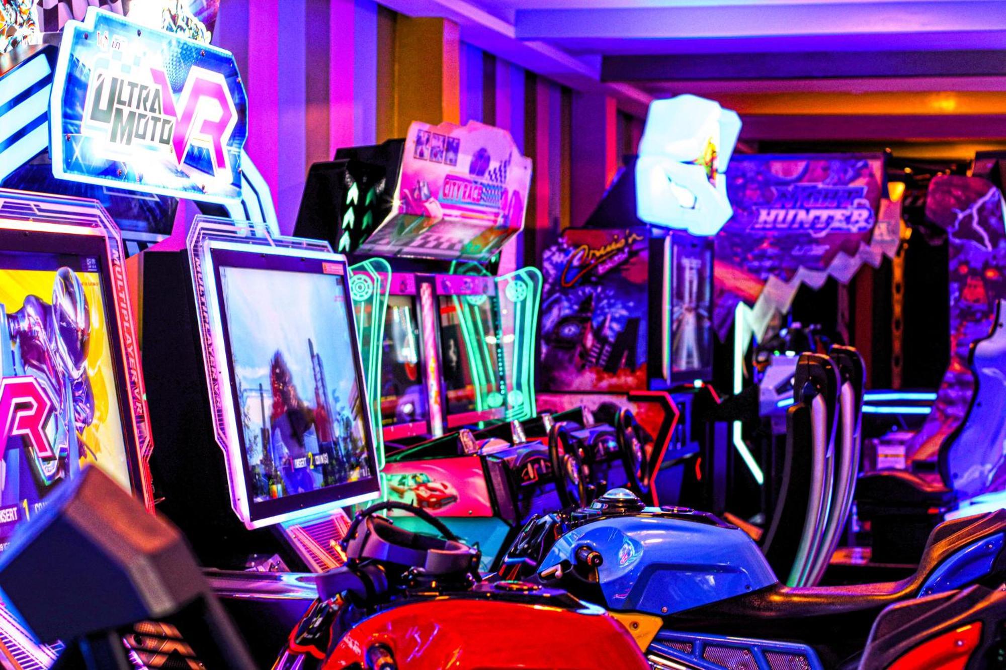 Lagoona Beach Luxury Resort And Spa Манама Екстериор снимка The photo shows a vibrant arcade scene featuring various arcade gaming machines. The machines are lined up, showcasing colorful screens and bright, neon lights, creating an energetic atmosphere. Some machines appear to be racing games, as indicated b