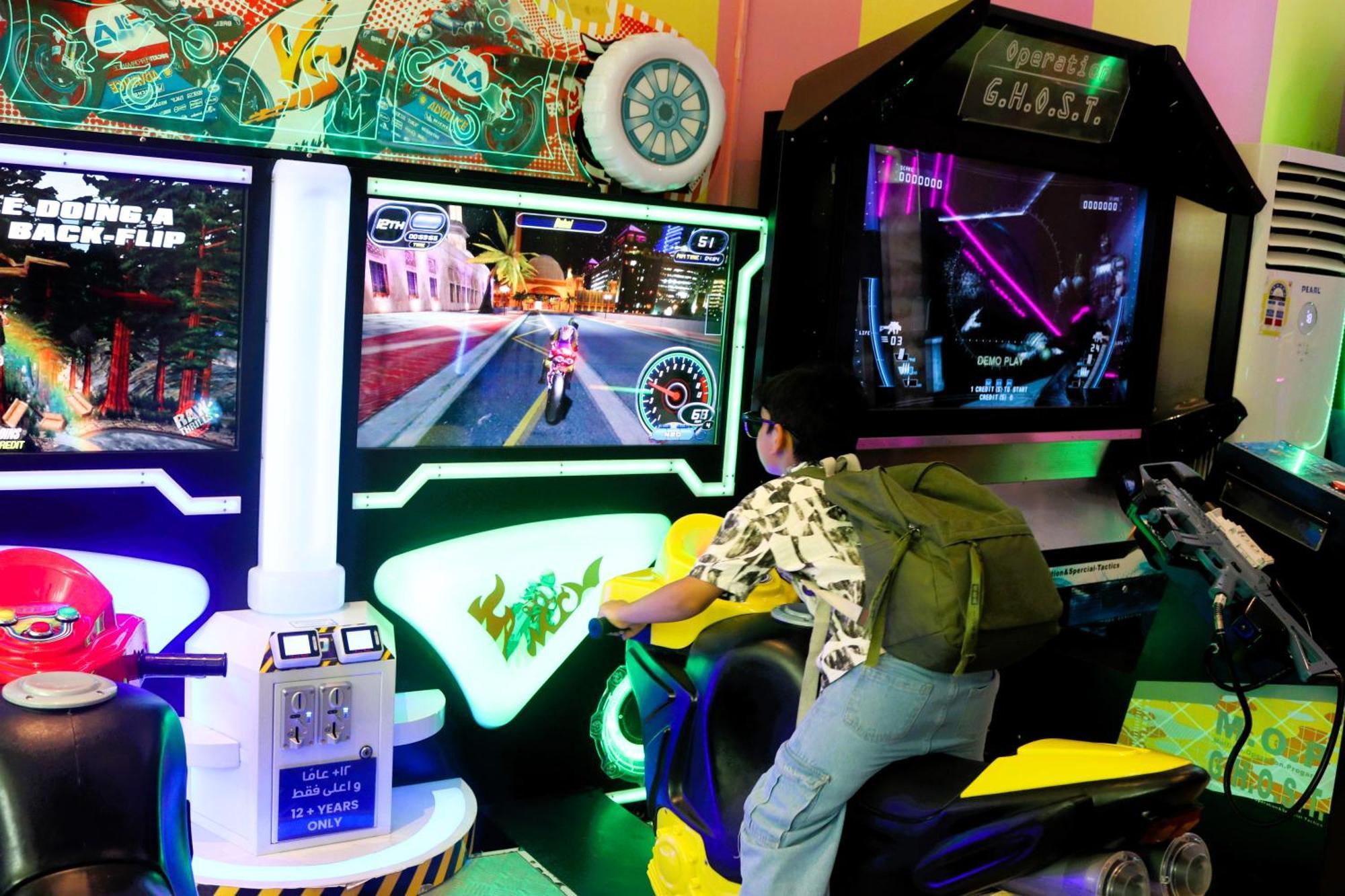 Lagoona Beach Luxury Resort And Spa Манама Екстериор снимка The photo shows a person playing an arcade motorcycle racing game. They are seated on a motorcycle-shaped seat, actively engaging with the game displayed on the screen in front of them. The screen shows a vibrant racing scene with streets and colorfu