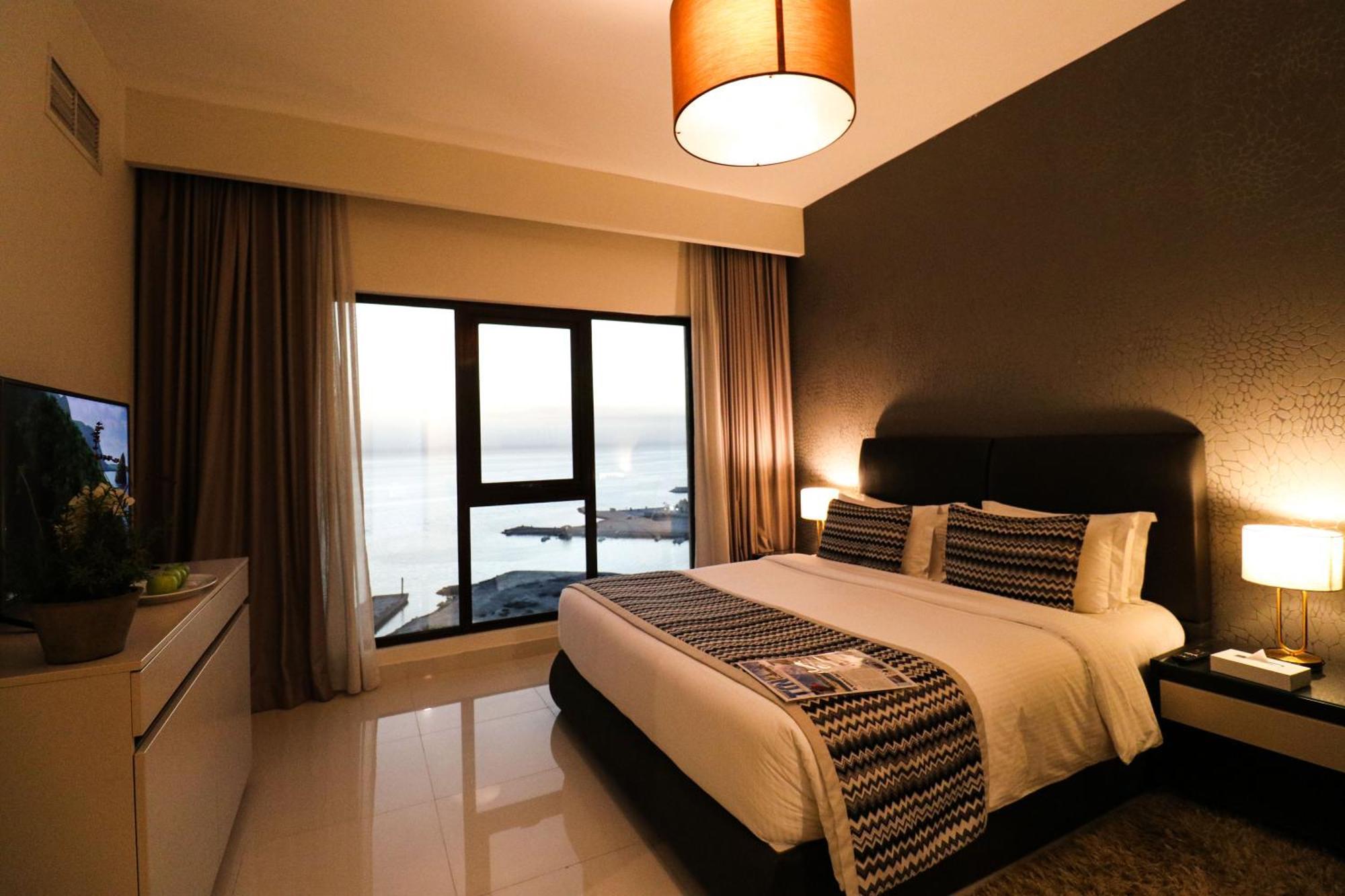 Lagoona Beach Luxury Resort And Spa Манама Екстериор снимка The photo shows a modern hotel room featuring a neatly made bed with decorative pillows. The room has a stylish design with a dark accent wall and a large window that offers a view of the outdoors. Natural light comes in, giving the space a bright an