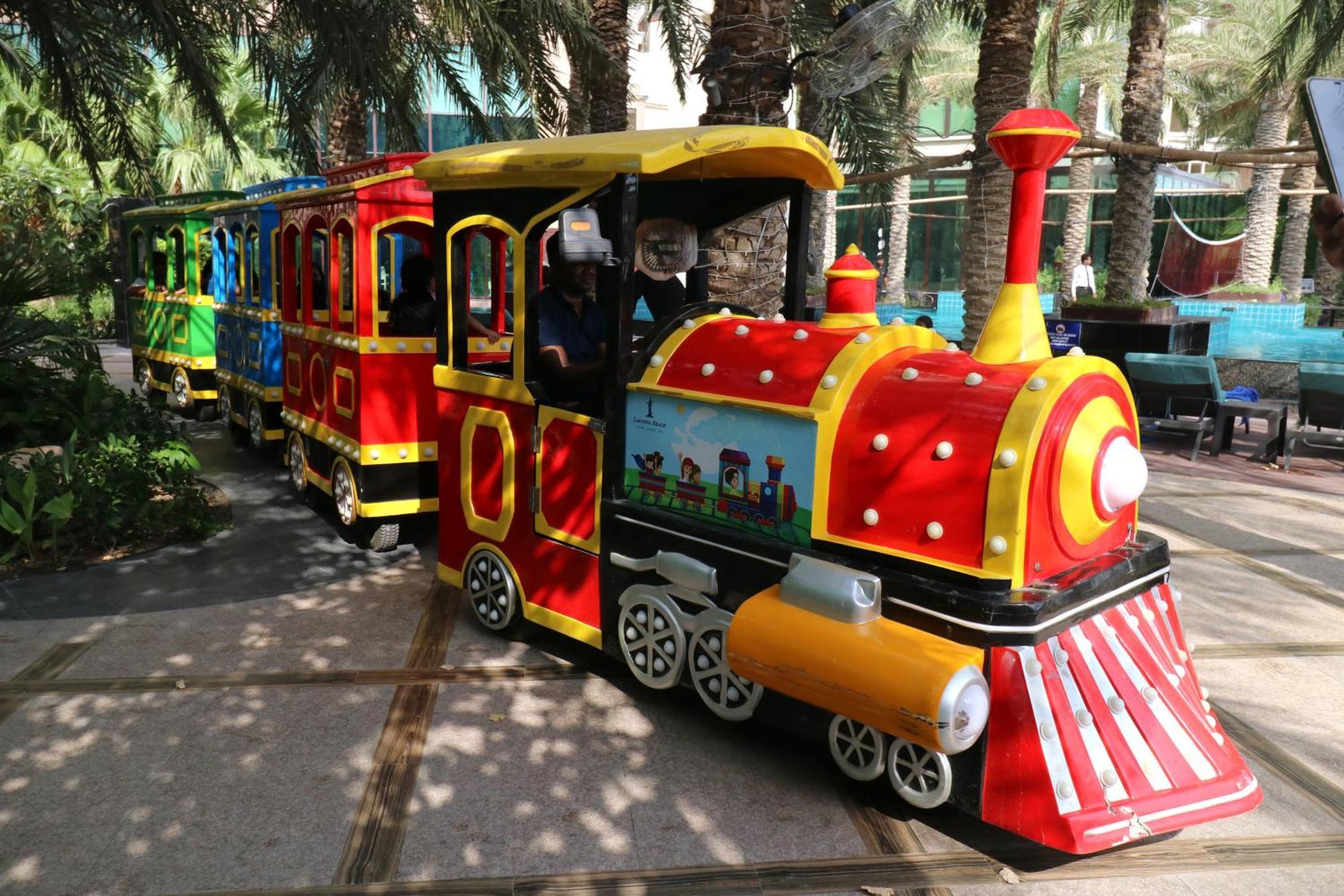 Lagoona Beach Luxury Resort And Spa Манама Екстериор снимка The photo shows a colorful miniature train. It features a vibrant design with bright red, yellow, and blue colors. The front of the train resembles a classic steam engine, complete with a prominent smokestack. The train is designed to resemble a fun 
