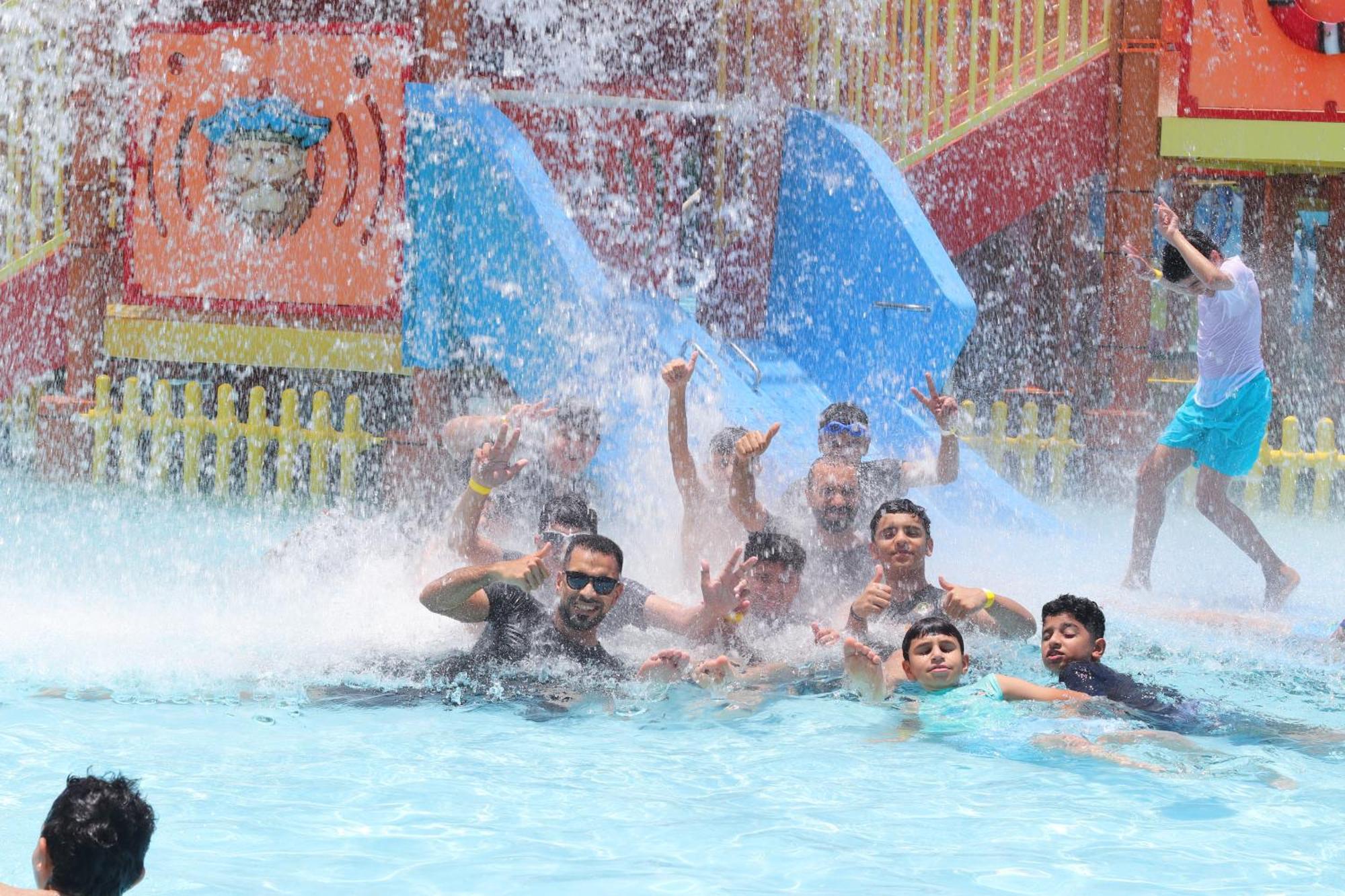 Lagoona Beach Luxury Resort And Spa Манама Екстериор снимка The photo shows a lively scene at a water park or pool area. Several people, including adults and children, are enjoying themselves in the water, splashing and posing for the camera. Water is cascading down, creating a refreshing atmosphere. In the b