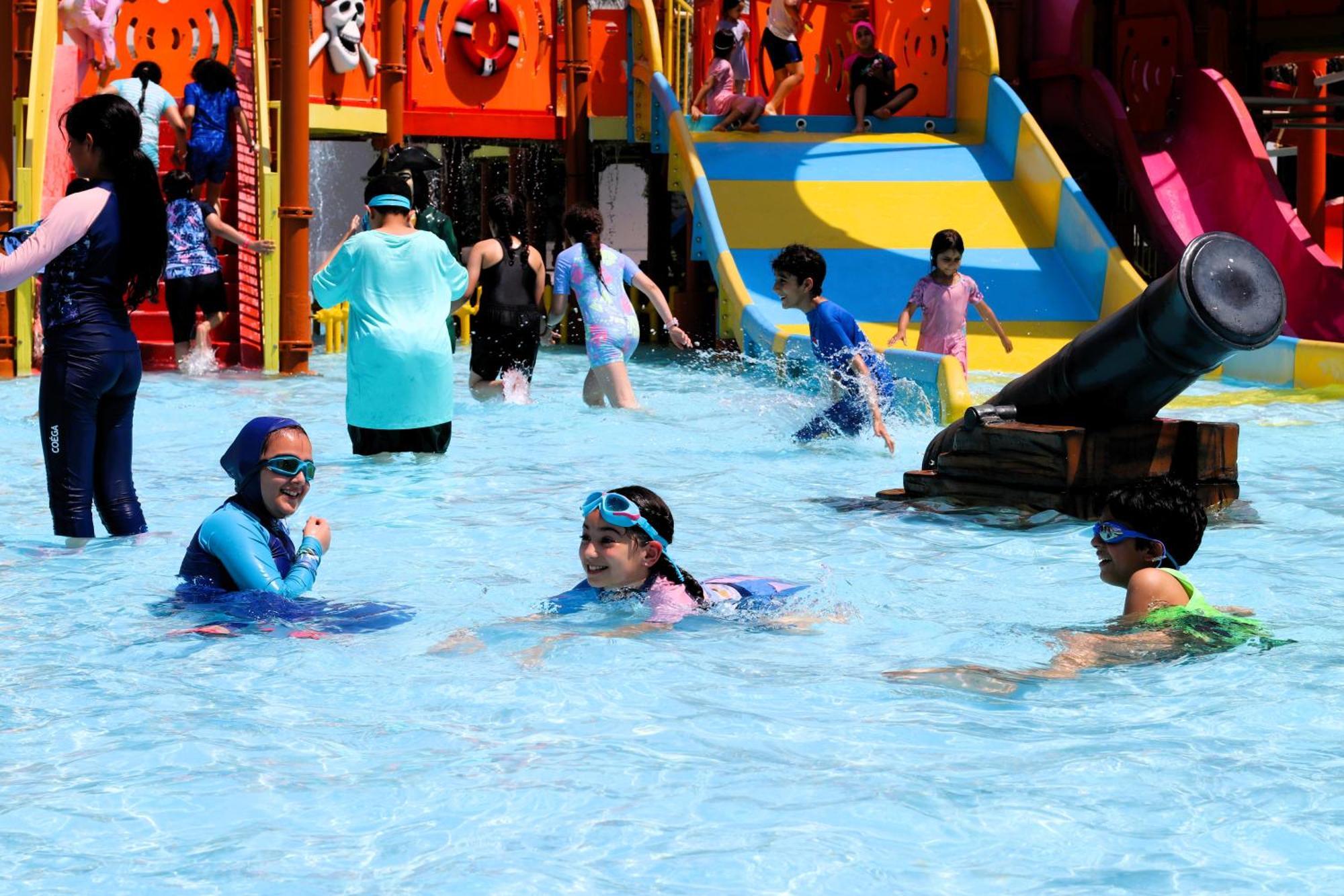 Lagoona Beach Luxury Resort And Spa Манама Екстериор снимка The photo shows a vibrant water park scene with several children playing in a shallow pool. Some are swimming and splashing around, while others are playing on colorful slides in the background. The atmosphere is lively and cheerful, with kids of var