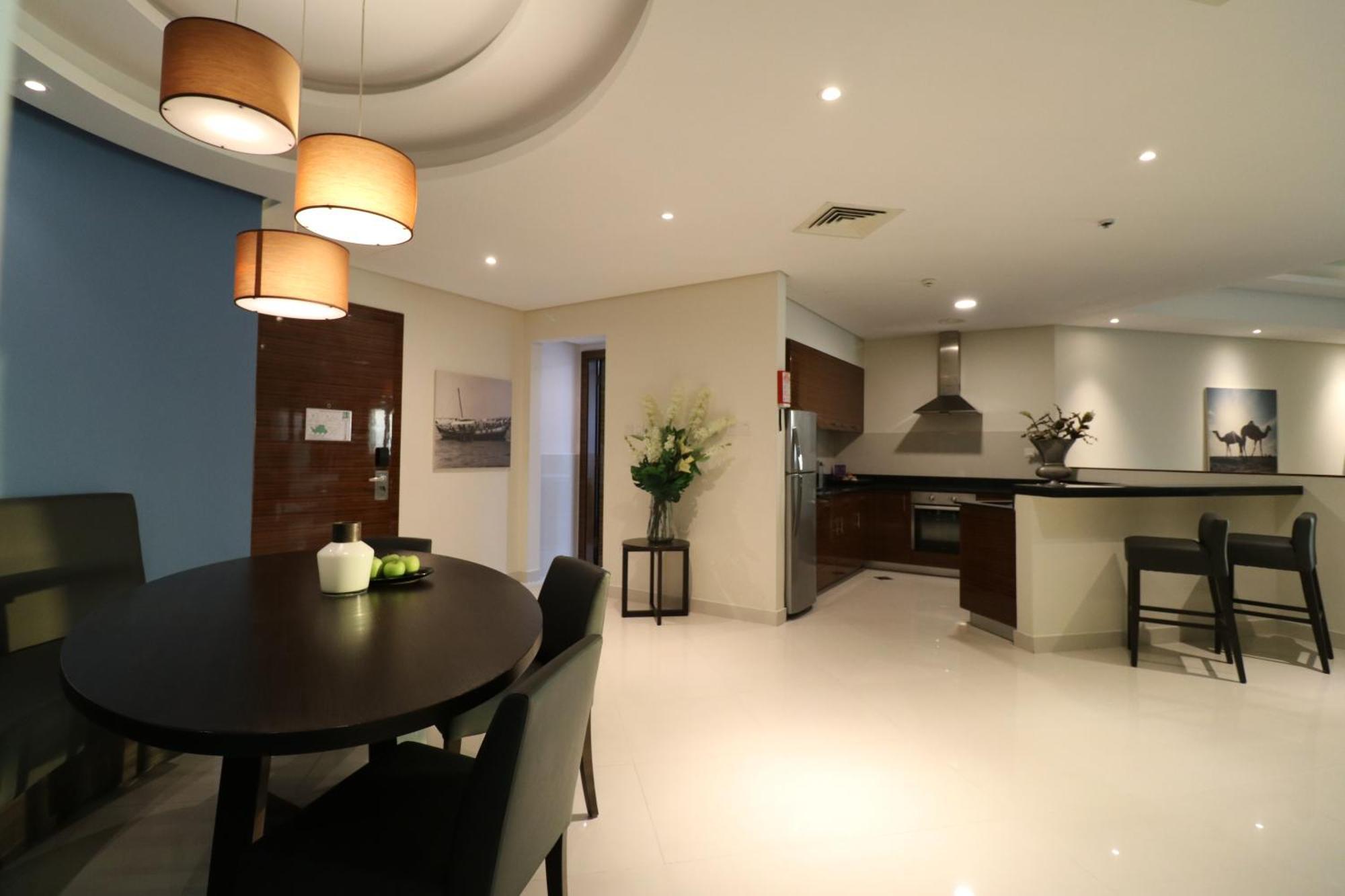 Lagoona Beach Luxury Resort And Spa Манама Екстериор снимка The photo shows a modern, open-concept dining and kitchen area. On the left, there is a round dining table with black chairs, accompanied by a few decorative elements like a small vase and some fruit. The walls have a combination of light and dark to