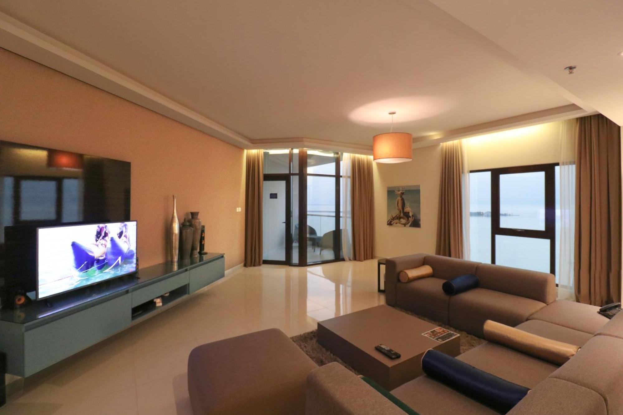 Lagoona Beach Luxury Resort And Spa Манама Екстериор снимка The photo shows a modern living room with a sleek design. There is a large wall-mounted television on a contemporary entertainment unit, with decorative items placed beside it. The room features a comfortable sectional sofa in light tones, with a cof