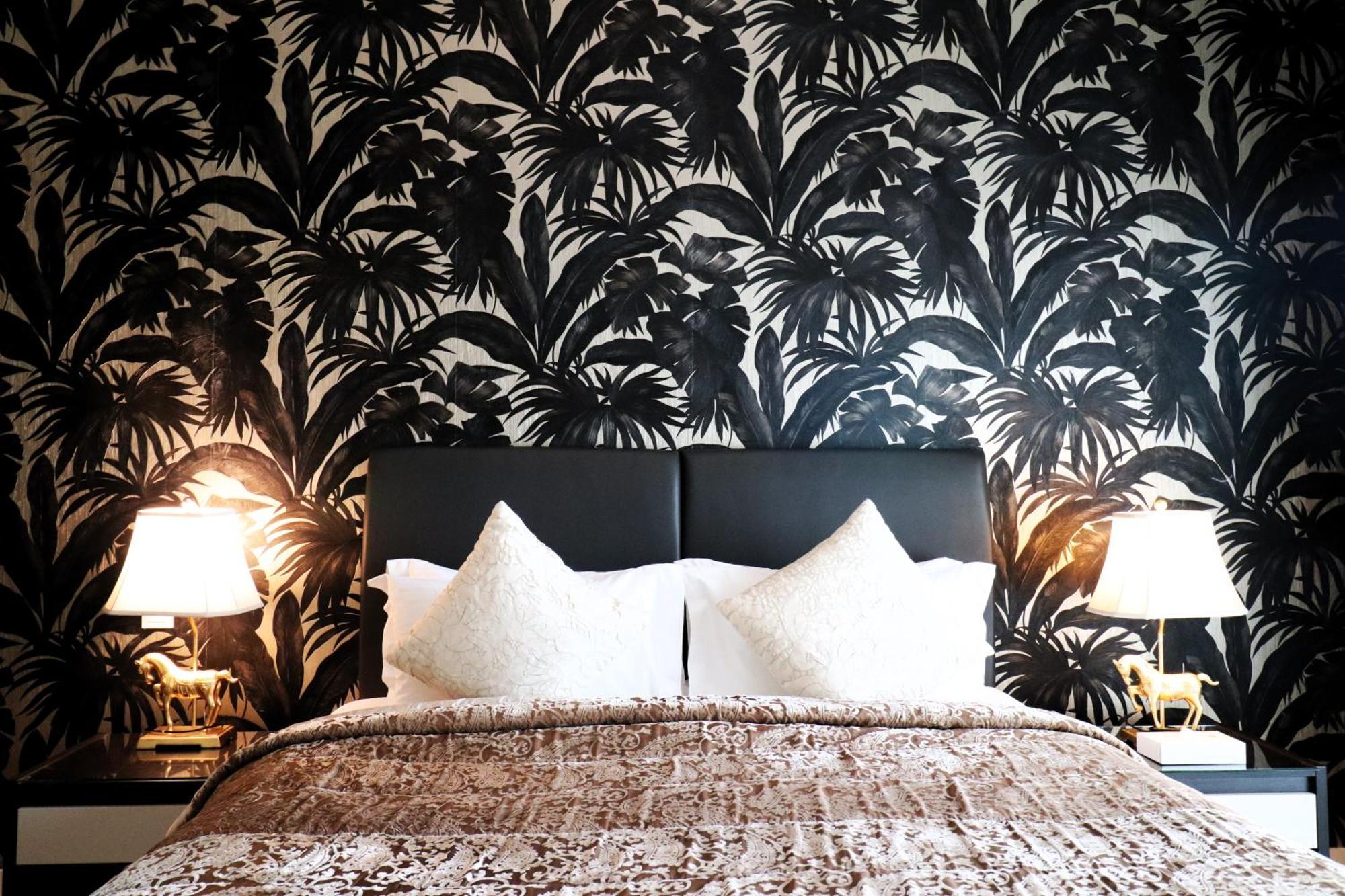 Lagoona Beach Luxury Resort And Spa Манама Екстериор снимка The photo depicts a stylish bedroom featuring a distinctive wall covered in a black and white tropical foliage wallpaper. The bed has a modern black headboard and is adorned with white pillows, creating a clean and elegant look. A textured brown thro