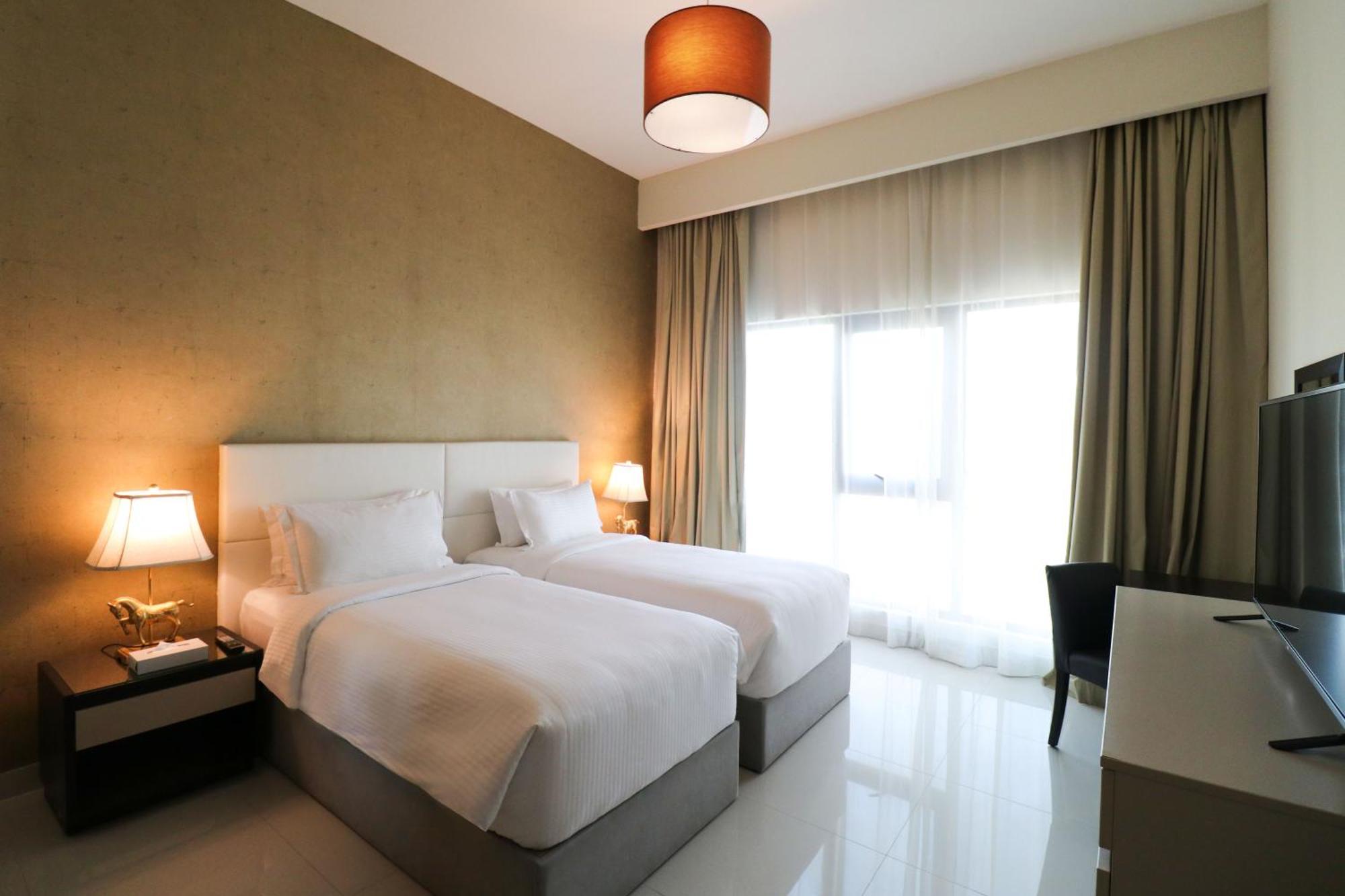Lagoona Beach Luxury Resort And Spa Манама Екстериор снимка The photo shows a hotel room featuring two single beds with white bedding. The walls have a neutral tone, and there's a large window covered by light, sheer curtains allowing natural light to enter. On either side of the beds, there are bedside table