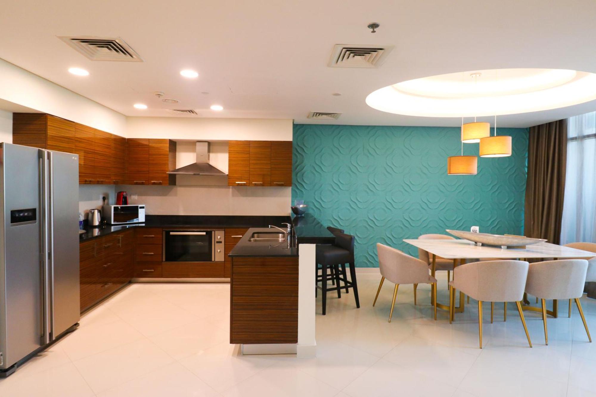 Lagoona Beach Luxury Resort And Spa Манама Екстериор снимка The photo shows a modern kitchen and dining area. The kitchen features wooden cabinets, sleek appliances including a stainless steel refrigerator, microwave, and an oven. There is a dark countertop and a small breakfast bar with high stools. The wall